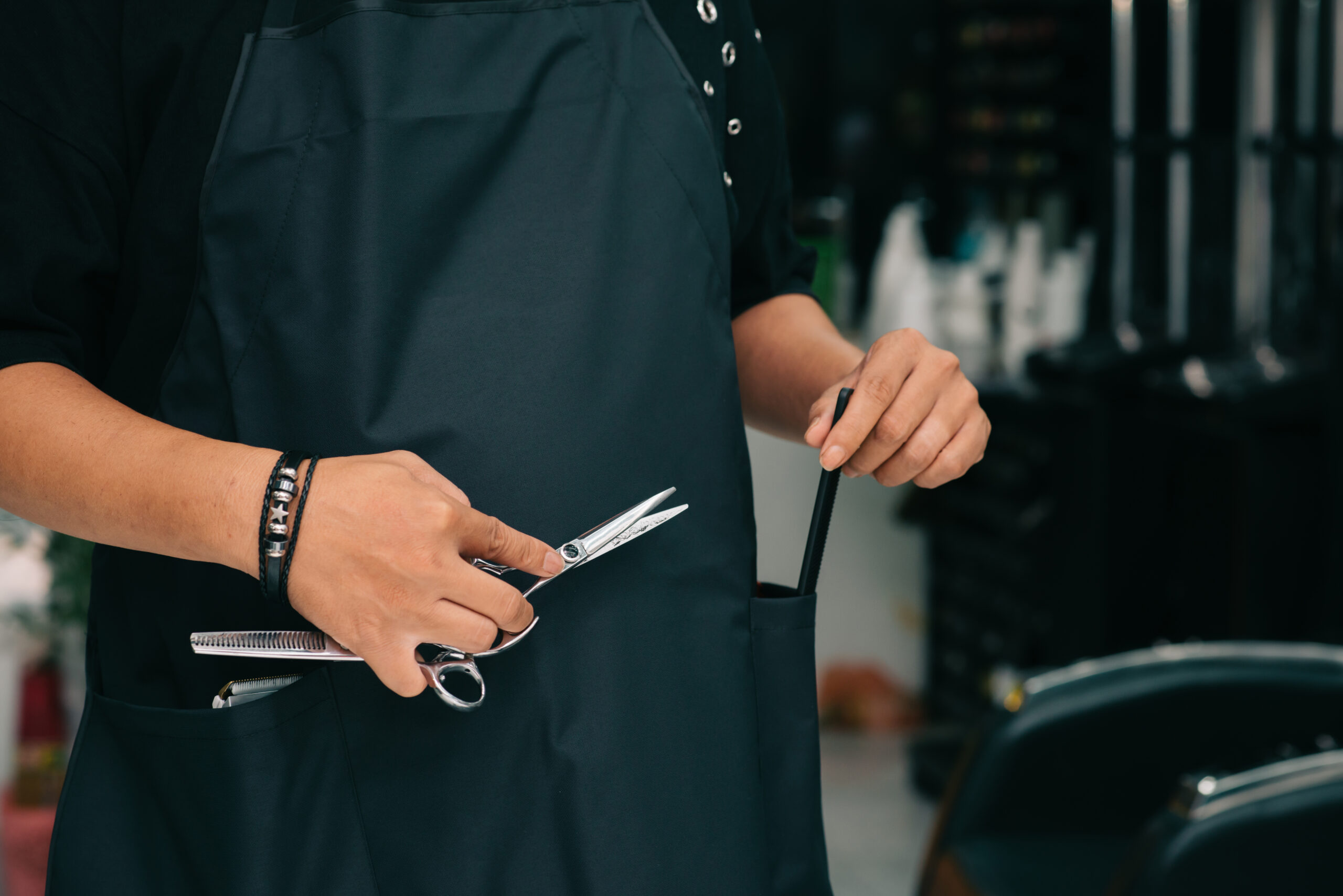 Cropped image of barber with two scissors and comb in his hands